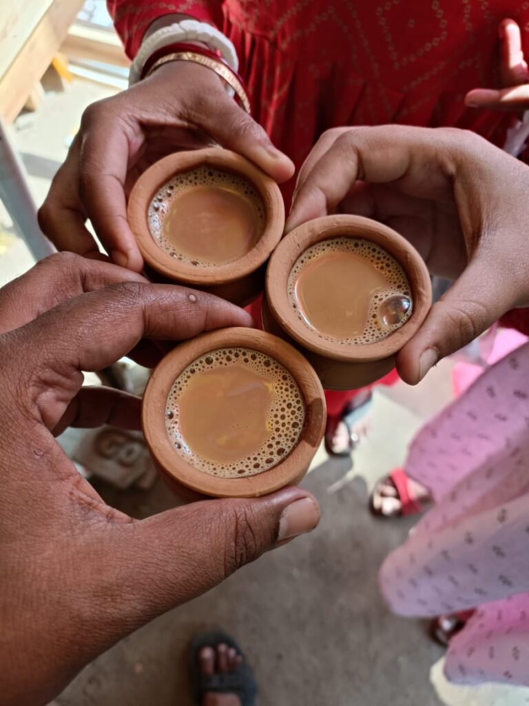 A top-down view of three people holding traditional clay cups (bhar) of hot tea during a trip to West Bengal.